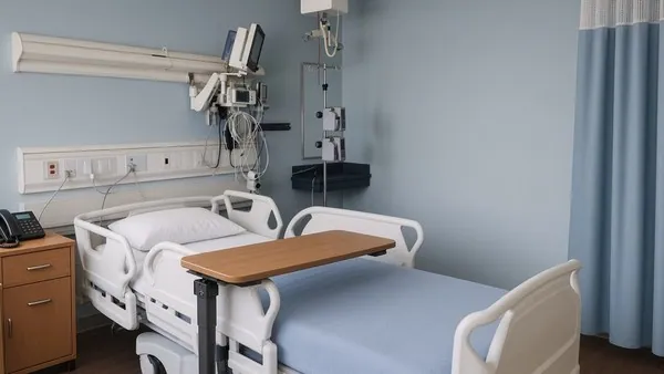 An empty hospital room with a made bed, an overbed tray table and an IV pole