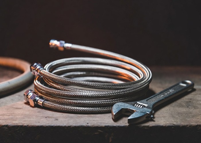 A coil of new braided stainless steel supply line on a workbench with an adjustable wrench beside it