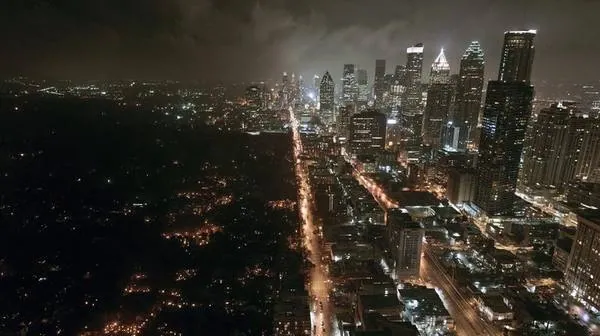 Aerial view of major American city at night with half completely dark and half fully lit showing rolling blackout