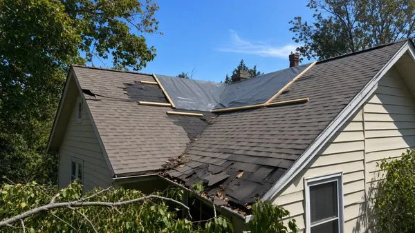 A grey tarp battened over a damaged patch of roof shingles near the ridge