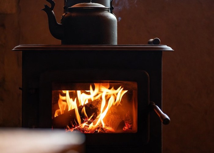 A wood stove burning with a kettle steaming on top of it