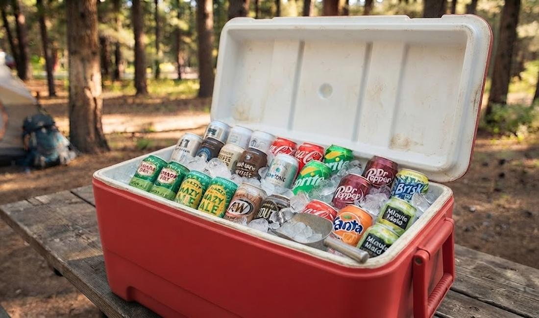 Standard hard-sided cooler open and packed with ice and cans at a campsite — the workhorse budget cooler for most households