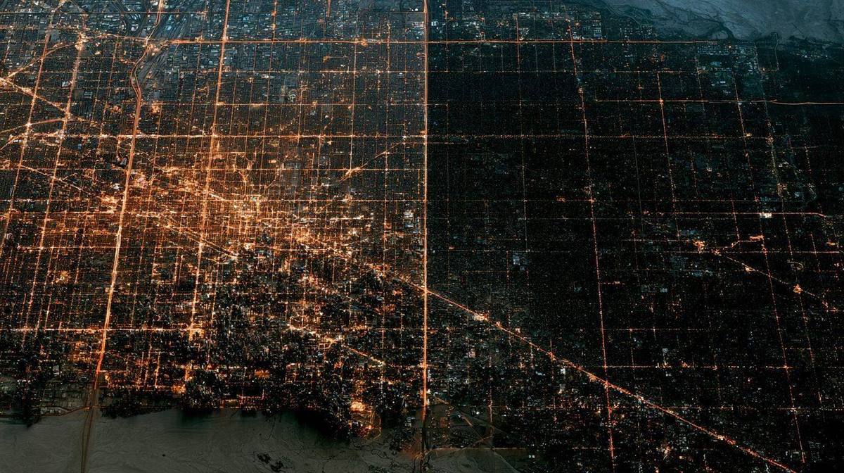 Satellite view of a large city at night with half the city lit and half in complete darkness during a rolling blackout