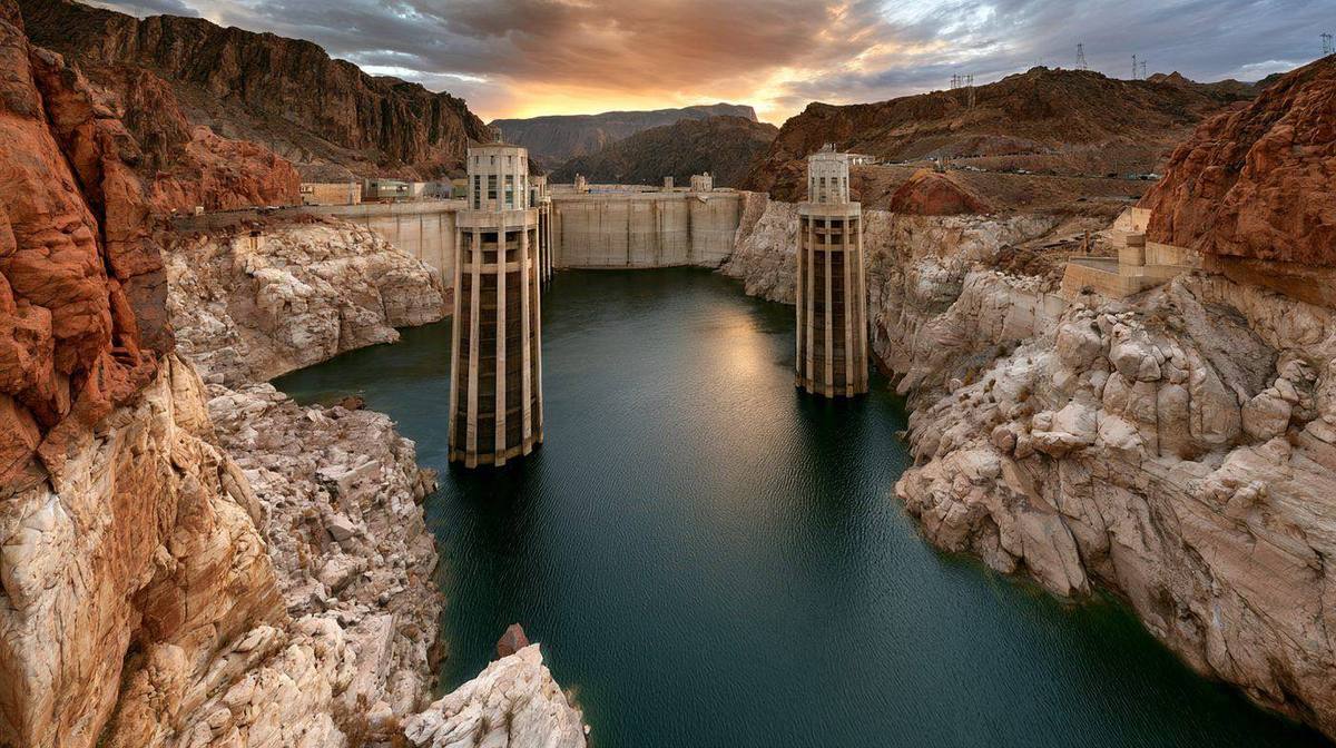 Large concrete hydroelectric dam with dramatic bathtub ring showing record low reservoir water levels from drought