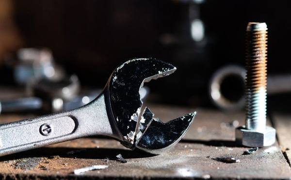 Cheap wrench shattered at the open end on a workshop bench next to a bolt — the result of inferior steel under load