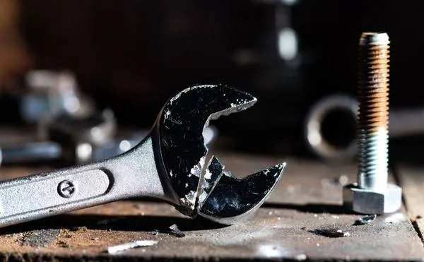 Cheap wrench shattered at the open end on a workshop bench next to a bolt — the result of inferior steel under load