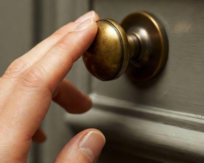 Two fingertips pinching a small round brass knob — the most fragile grip in the house
