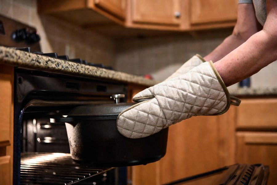 Lifting a cast iron Dutch oven from a low open oven wearing a thick quilted oven mitt, the pot supported close to the body