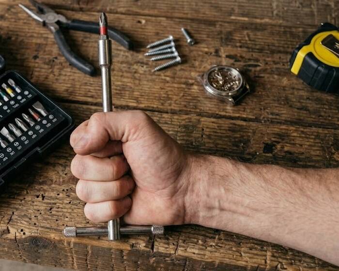 A closed fist gripping a screwdriver handle over a wooden workbench
