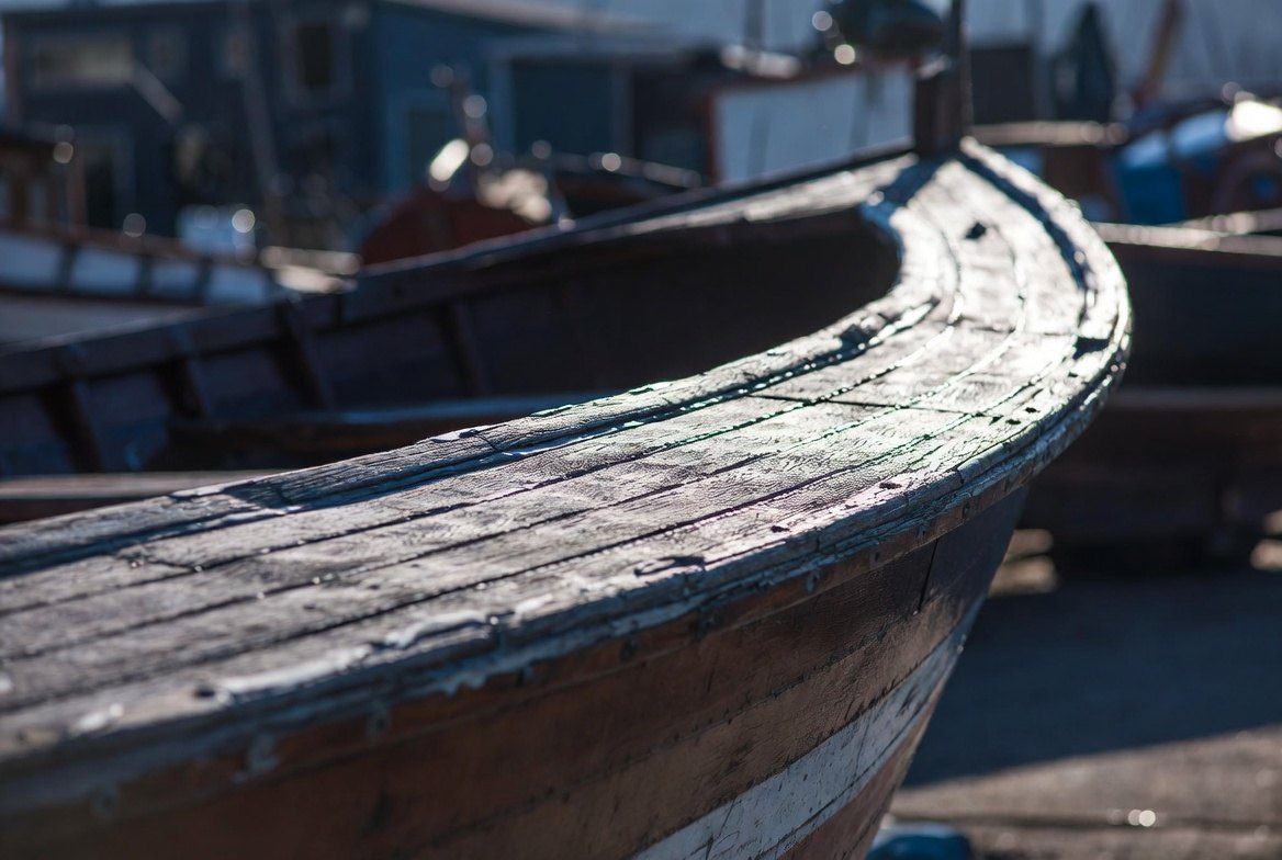 Close view along the weathered sheer of an old wooden boat, paint worn back to bare grain, fastenings visible