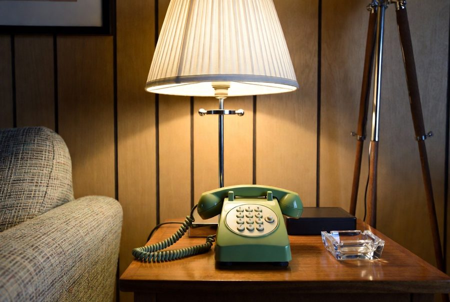 Green corded push-button telephone with a curly wire on a wood side table under a lamp — the phone that works when the power is out