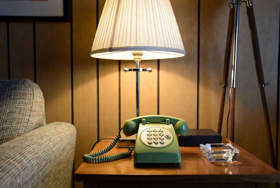 Green corded push-button telephone with a curly wire on a wood side table under a lamp — the phone that works when the power is out