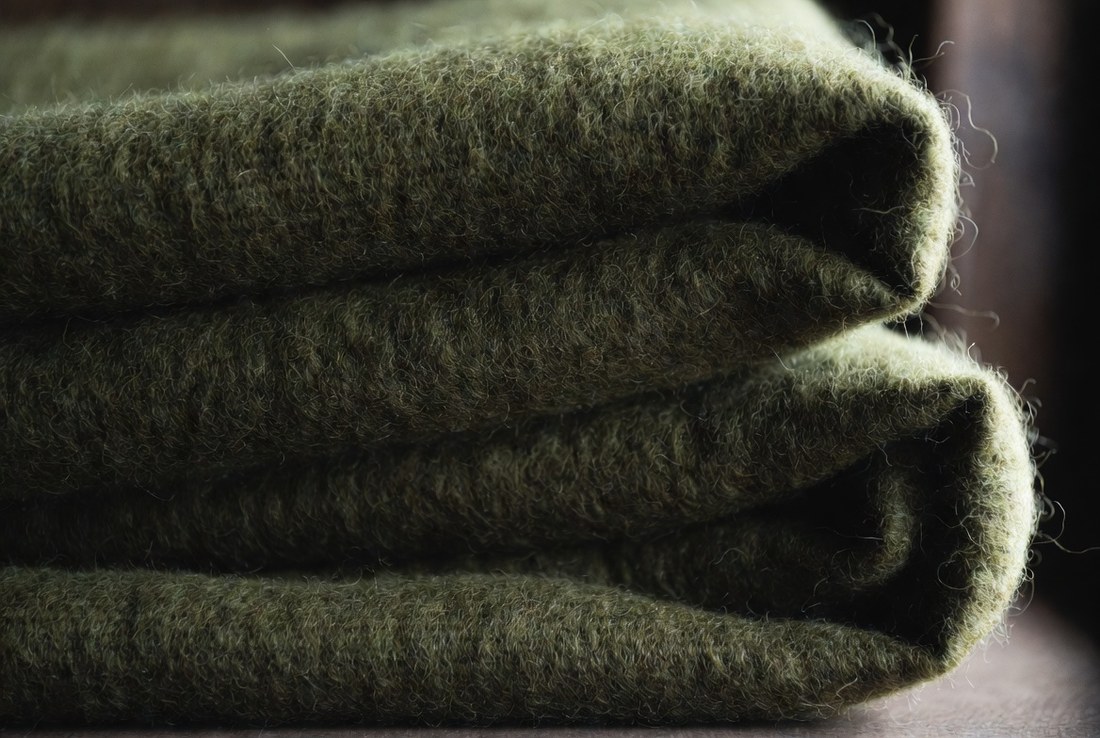 Extreme close-up of folded coarse olive wool blanket cloth, the crimped fibers and open weave clearly visible