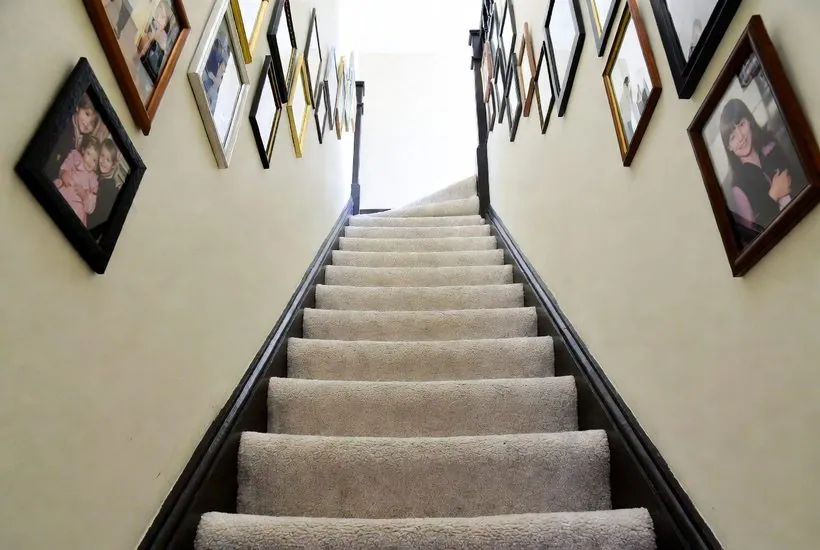 A carpeted staircase seen from the bottom, treads and risers all the same pale cream, with the edge of each step hard to make out