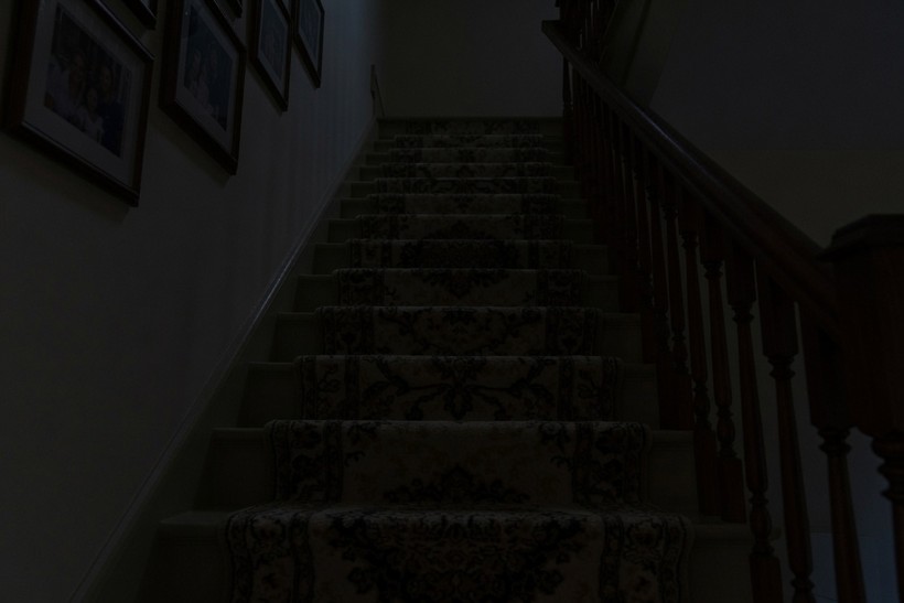 The same carpeted staircase at night with no lighting at all, the treads barely distinguishable in the dark